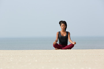 Fototapeta na wymiar African american woman sitting at beach in yoga pose