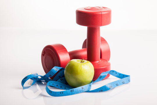 Red dumbbells weight with measuring tape and green apple