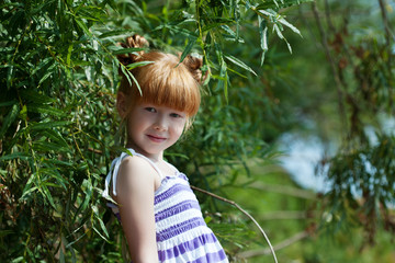 Cute red-haired little girl posing near tree
