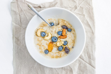 Oat porridge with fresh blueberry, nuts and honey in a white cer