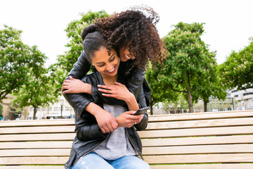 Best friends chatting with smartphone on park bench