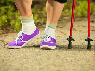 Plakat active senior legs in sneakers nordic walking in a park.