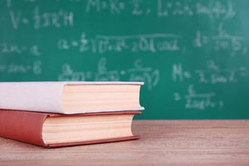 Books on wooden table on blackboard background