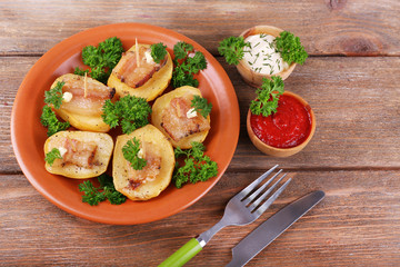 Baked potato with bacon on plate, on wooden background