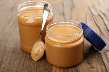 Creamy peanut butter in jar, on wooden table