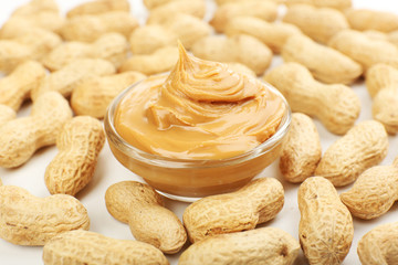 Creamy peanut butter in bowl on peanut background, close-up