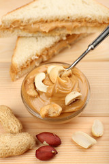 Creamy peanut butter in bowl and bread slices on wooden table