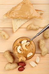 Creamy peanut butter in bowl and bread slices on wooden table