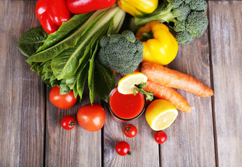 Tomato juice in glass and fresh vegetables on wooden background