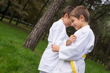 Two kids practicing judo outdoors in a park.