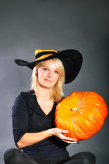 Pretty blonde woman in a costume of witch posing with pumpkins