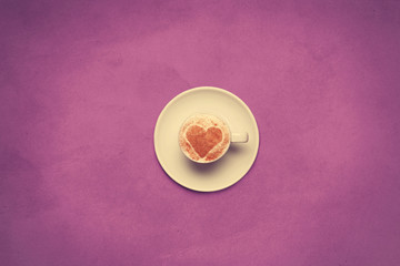 Cup of coffee with heart shape symbol on color background.