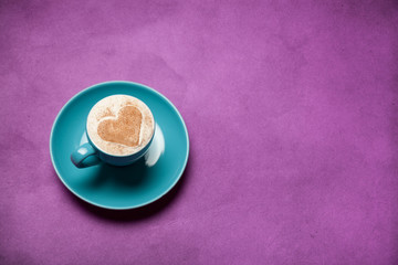 Cup of coffee with heart shape symbol on color background.