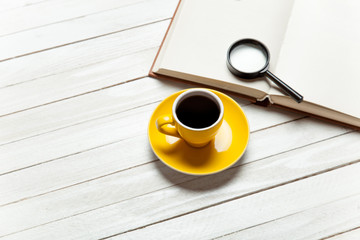 Cup of coffee and book with loupe on wooden table.