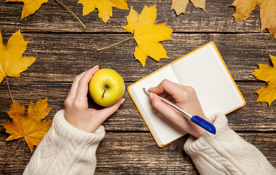Female hand writing something in to notebook and holding apple