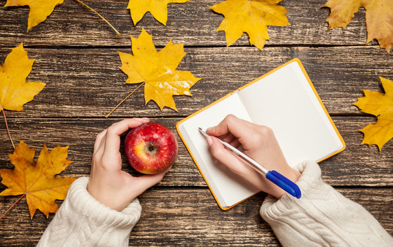 Female hand writing something in to notebook and holding apple
