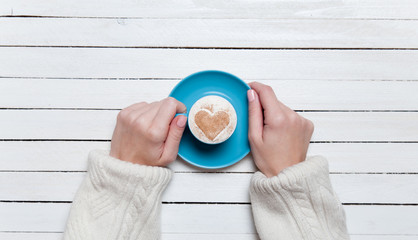 Female hands holding cup of coffee on wooden table.