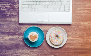 Cup of coffee and donut with notebook on a table.
