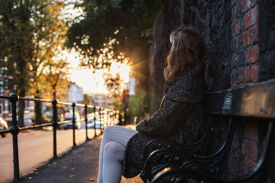 Young woman sitting on bench at sunset