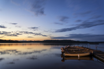Fototapeta na wymiar Beautiful landscape sunrise over still lake with boats on jetty