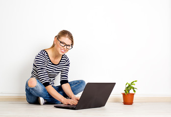 Young woman in eyeglasses sitting on bare floor with home plant