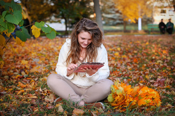 beautiful girl in autumn park with a tablet resting