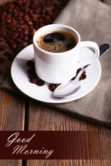 Cup of coffee and coffee beans on napkin on wooden background