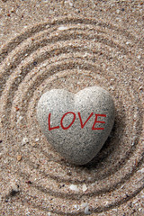 Fototapeta na wymiar Grey zen stone in shape of heart, on sand background