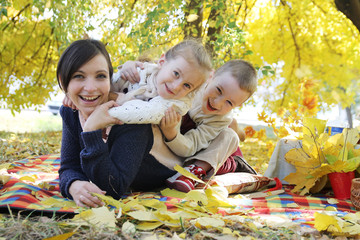 Happy children hugging their mother under autumn trees