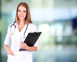 Young beautiful doctor holding folder on hospital background