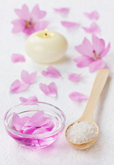 spa composition with sea salt in spoon, pink  petals and candl
