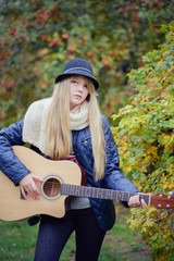 Fototapeta na wymiar young blonde teen girl playing guitar in the park
