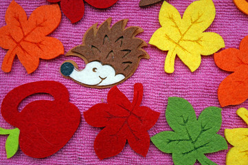 Hedgehog and colorful Maple leaves out of felt on a pink fabric