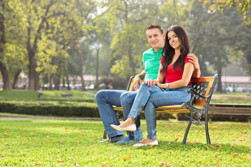 Young couple posing seated on a bench in park