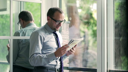 Happy businessman reading newspaper next to the window