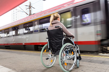Frau sitzt in einem Rollstuhl auf einem Bahnhof