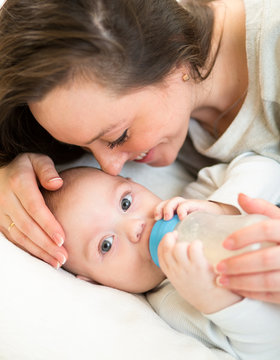 Loving mother at home feeding baby with a milk bottle