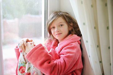 Beautiful little girl in bathrobe near window