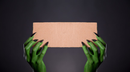 Green monster hands with black nails holding empty piece of card