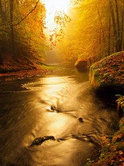 Stony bank of autumn mountain river covered by orange mist