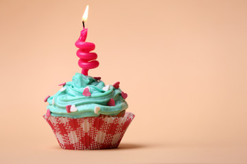 Delicious birthday cupcake on table on beige background