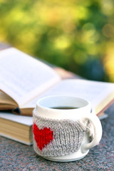 Cup with hot drink and book, outdoors