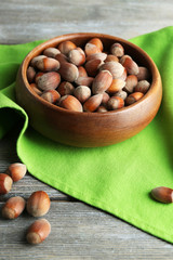 Hazelnuts in wooden bowl, on napkin on wooden background