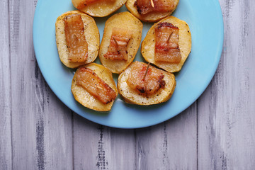 Baked potato with bacon on plate, on wooden background