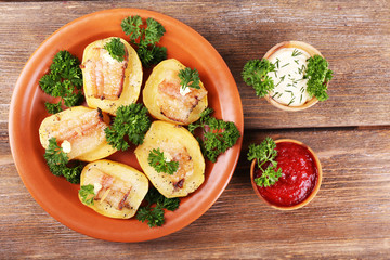 Baked potato with bacon on plate, on wooden background