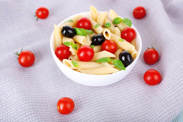 Fototapeta na wymiar Pasta with tomatoes, olives and basil leaves in bowl on napkin