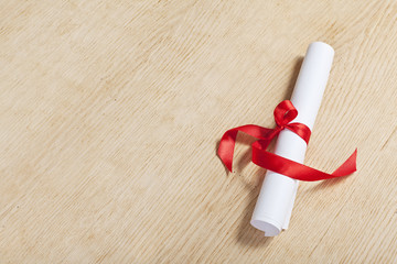 Scroll of paper with a red ribbon on a wooden surface.
