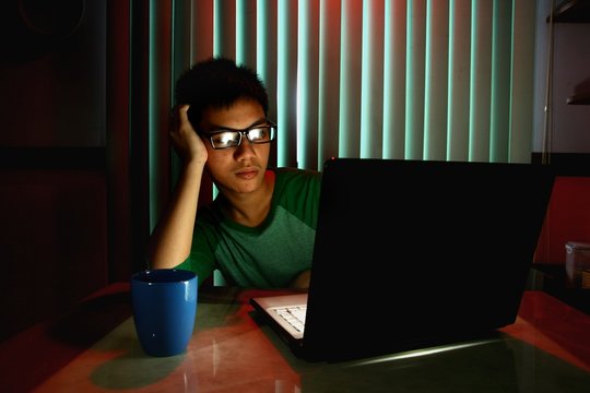 Teen with eyeglasses and bored in front of a laptop computer
