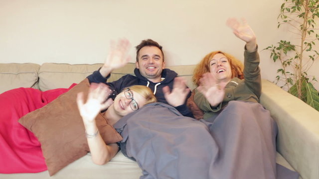Group of ecstatic friends waving and relaxing on the sofa at hom