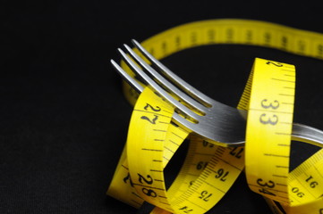 Measuring tape and fork on black background. Diet concept.
